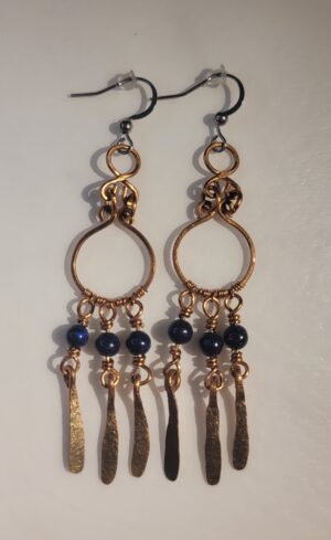 Käsintehdyt kuparikorvakorut, joissa on sinisiä lapis lazuli helmiä ja riippuvia kuparikoristeita.